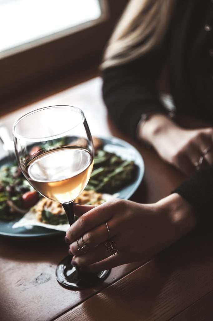 Female hand with glass of wine and food in the background